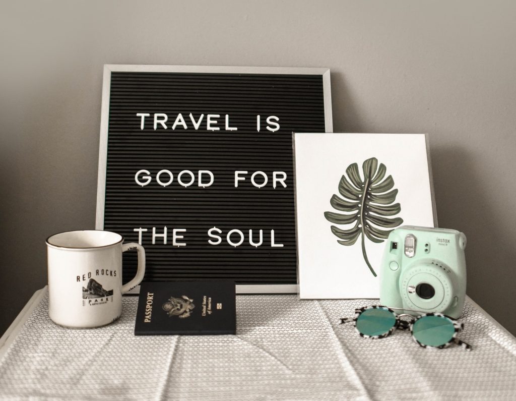 Styled travel flat lay featuring an instant camera and passport on a clean background.