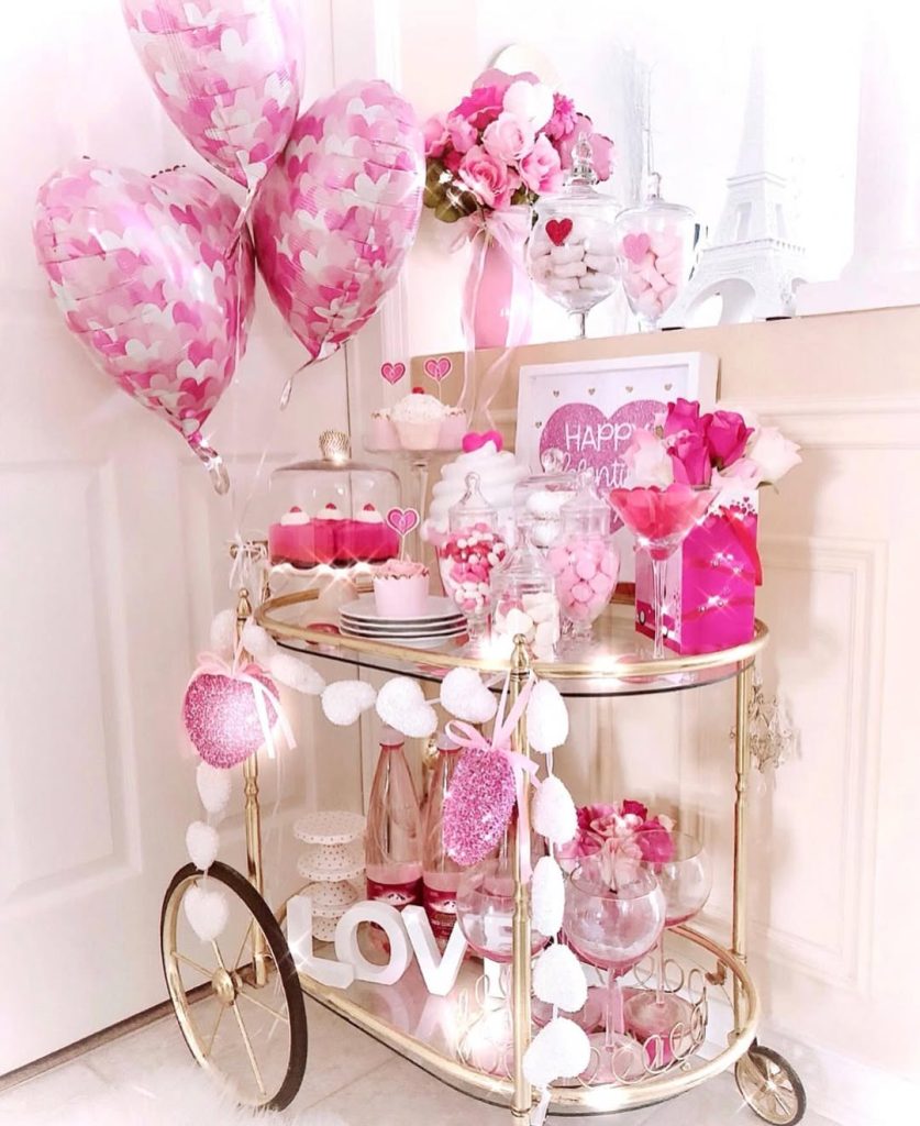 A decorated bar cart with pink heart balloons and Valentine's themed party supplies.
