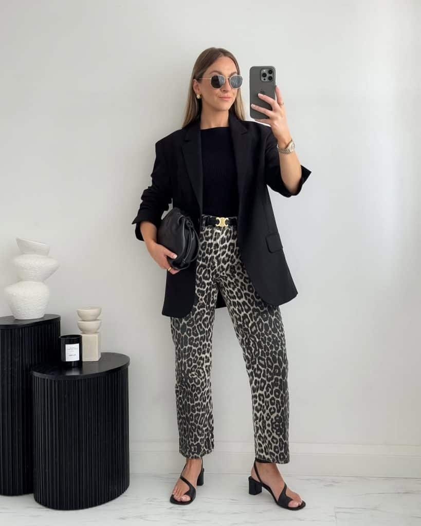 Mirror selfie of a woman wearing a black blazer over a black top and leopard-print trousers.