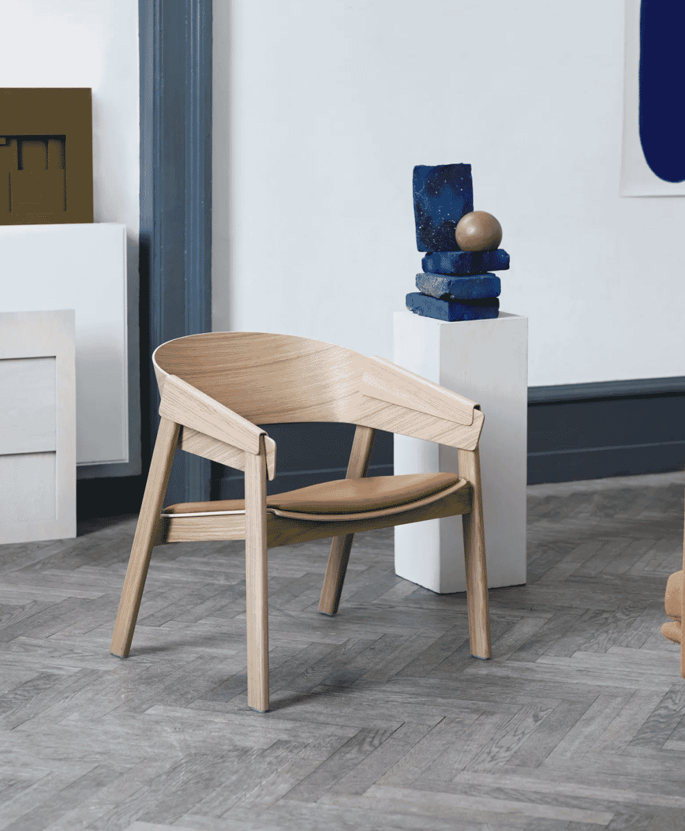 Modern wooden lounge chair with cognac leather seating on a classic herringbone wood floor.