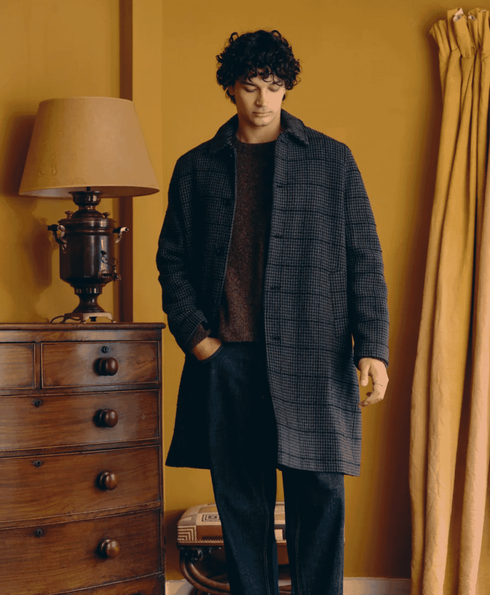 A man wearing a dark grey houndstooth wool coat in a vintage-style room.