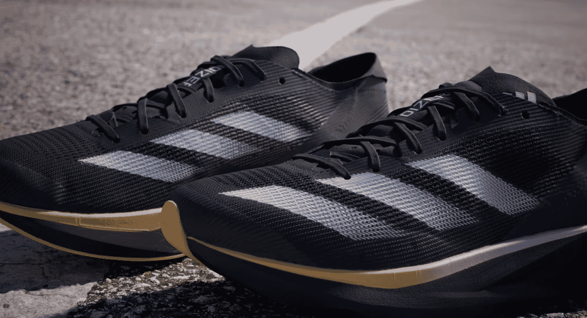 A pair of black Adidas running shoes with silver and gold accents on an asphalt road.