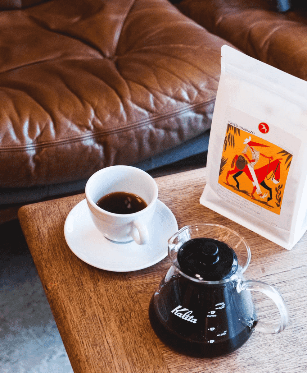 A close-up of an espresso cup and a specialty coffee setup on a wooden table.