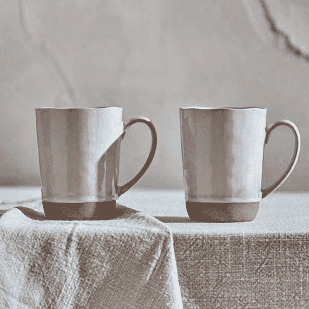 Two rustic ceramic mugs with textured surfaces sitting on a linen cloth.