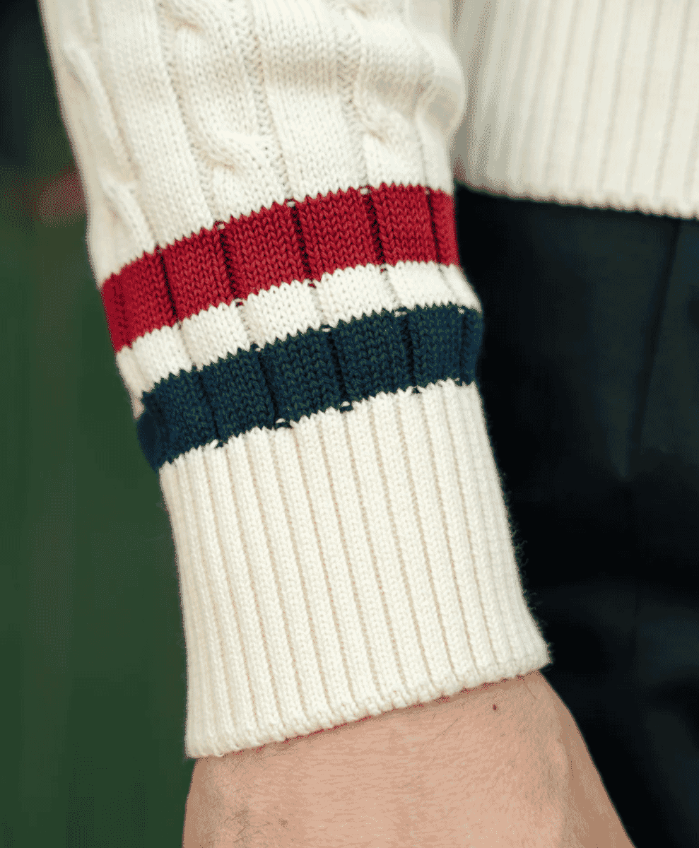 Close-up of cream cable-knit sweater texture and striped cuff detail.