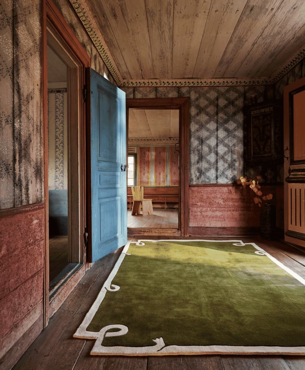 A vintage-style hallway with a large green rug featuring white decorative borders on wooden floors.