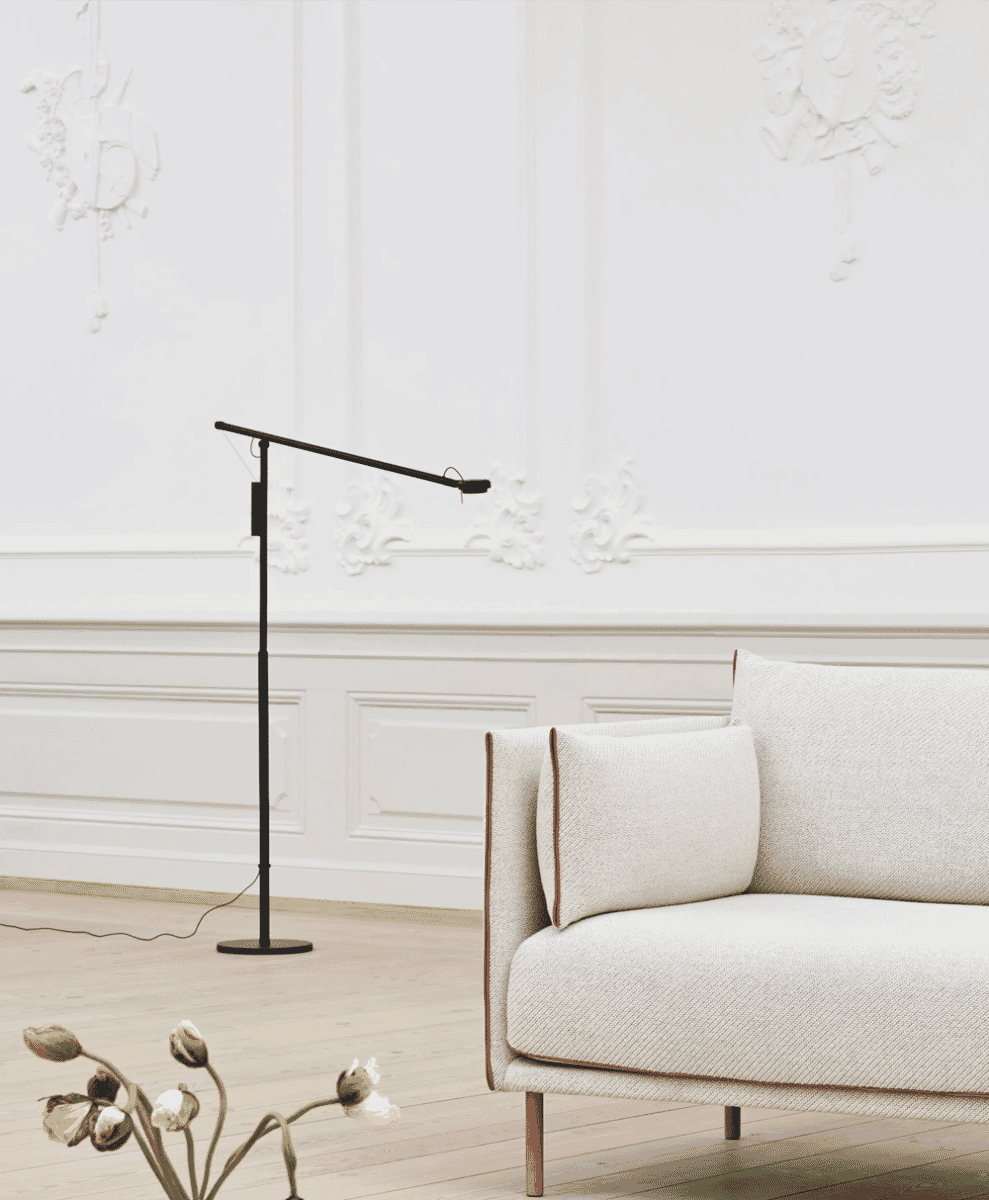A black adjustable floor lamp standing next to a beige textured sofa in an elegant room with white wall moldings.