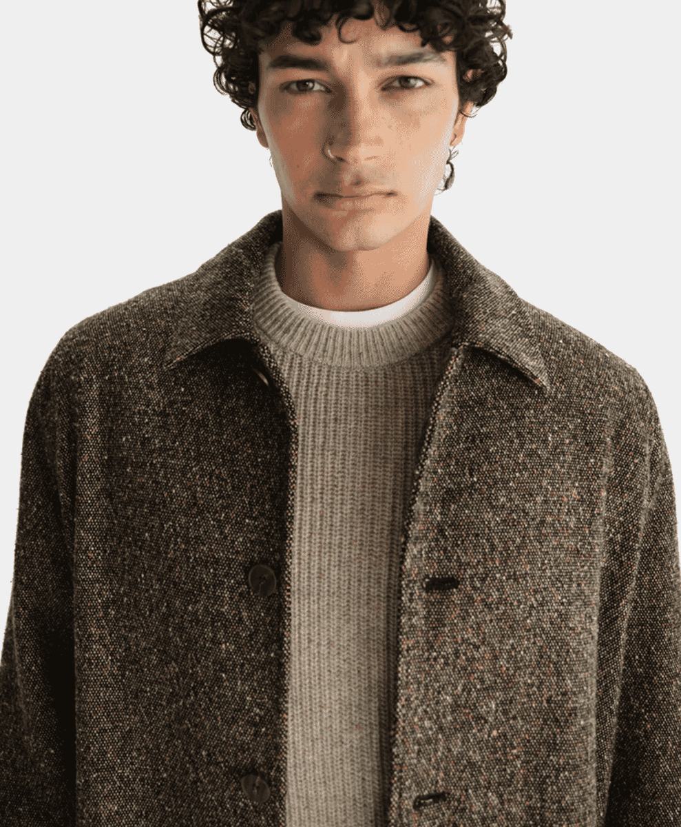 Close-up of a man wearing a brown wool coat over a cream ribbed sweater.
