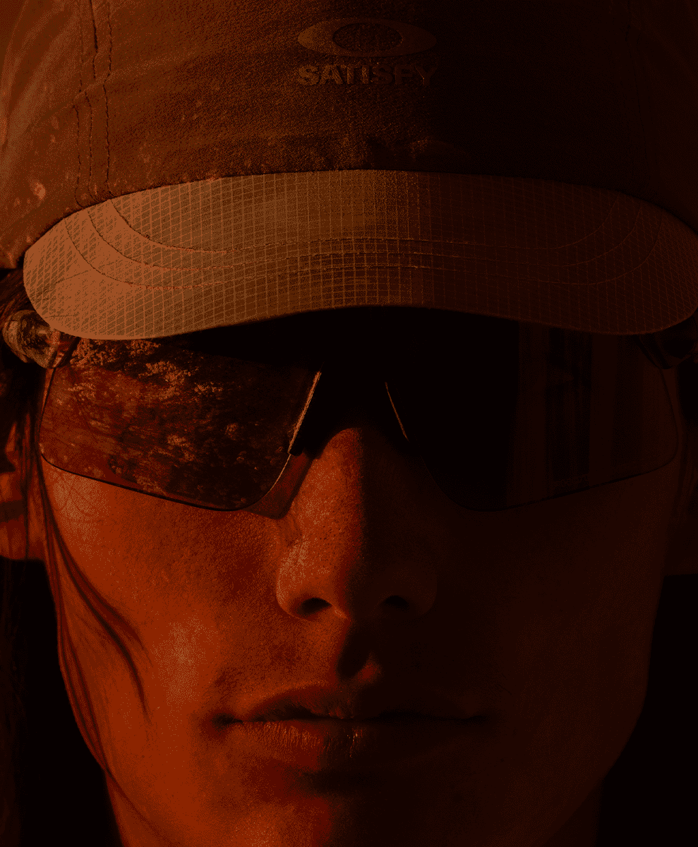 Close-up of a model wearing Oakley sunglasses in warm orange lighting.