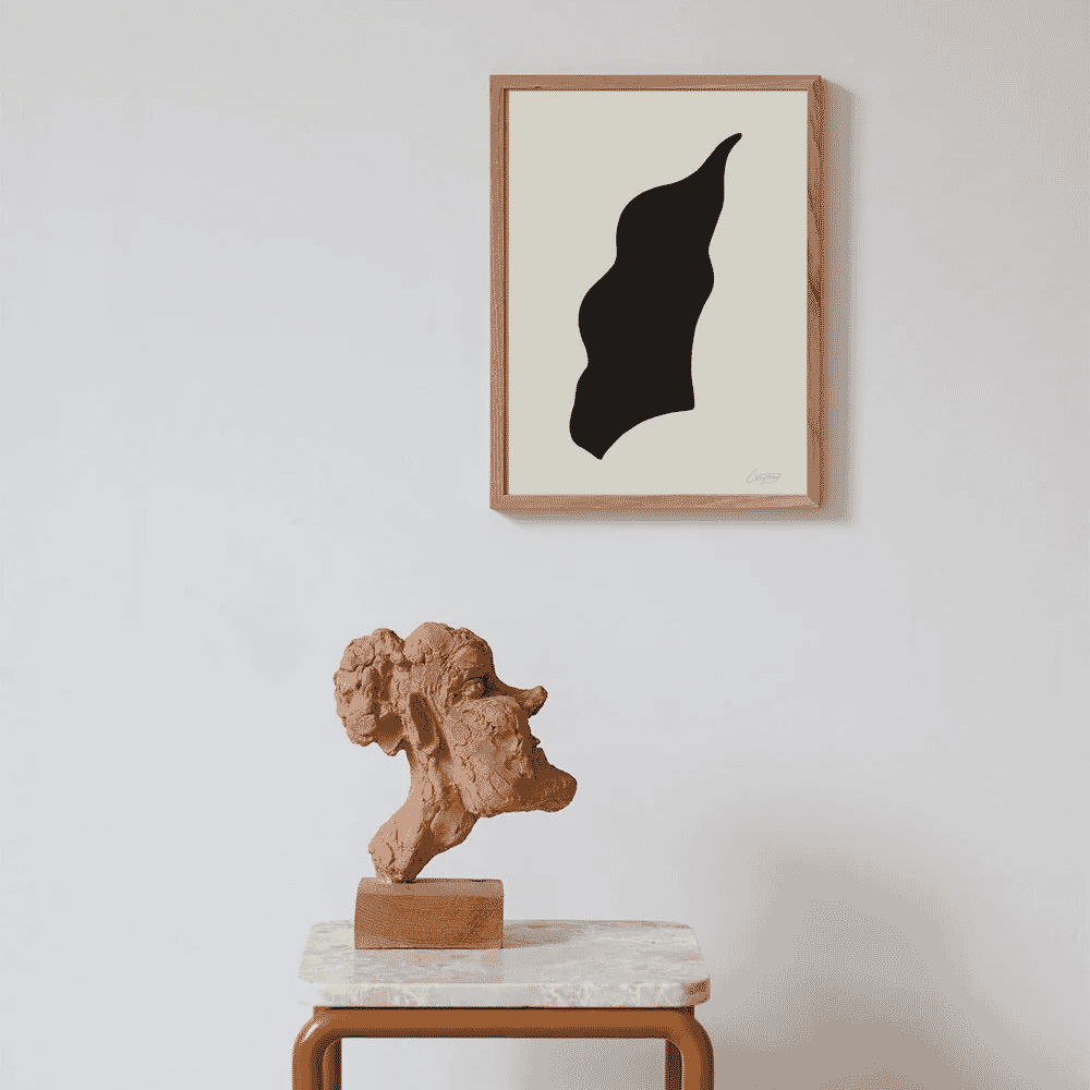A framed black organic silhouette artwork placed above a terracotta bust on a marble-topped table.