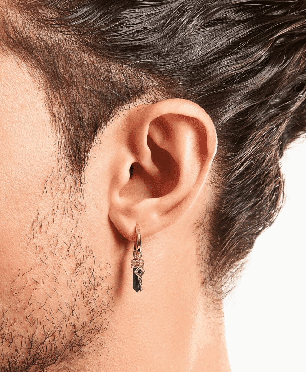 Close-up of a man's ear wearing a gold hoop with a black faceted pendant.